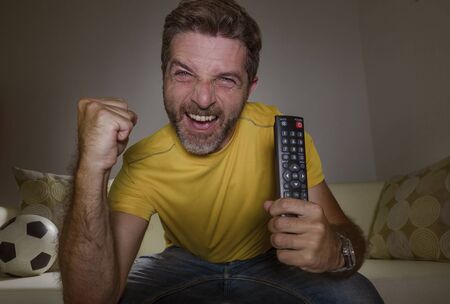 portrait at home of young happy and excited man watching European football game on TV celebrating goal on couch screaming spastic gesturing crazy cheerful as soccer fan enjoying victoryの写真素材