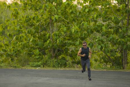 lifestyle portrait of young attractive and healthy man on his 30s or 40s running on country road...