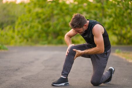 outdoors portrait of young attractive sport man in pain touching his knee suffering ligaments...