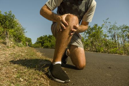 close up hands and legs of sport man injured touching his knee in pain suffering physical problem or some injury during running workout outdoors in sport accident and health care conceptの写真素材