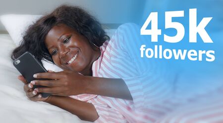 young cool and happy black African American woman lying relaxed on bed using internet mobile phone...