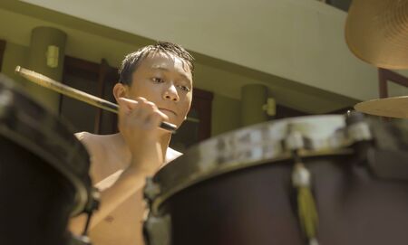 Asian American teenager playing dums. Summer portrait of handsome young boy practicing on drum kit at home garden rehearsing rock song enjoying his hobby in teen lifestyle conceptの写真素材