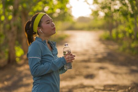 young Asian runner girl drinking water sweaty and tired. Attractive and exhausted Korean woman...