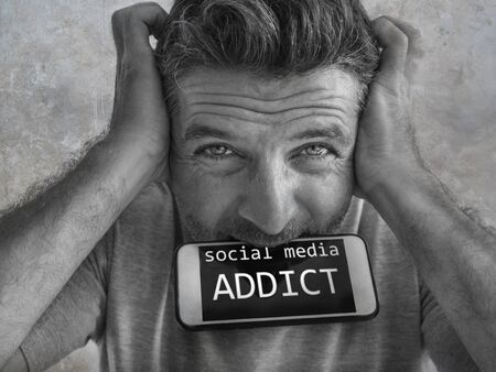 portrait of sick and crazy stressed man biting mobile phone screaming desperate and hysteric looking like a weirdo in internet and social media addiction concept isolated backgroundの写真素材