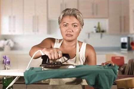 attractive upset and stressed woman 40s to 50s ironing tired and unhappy at home kitchen doing housework and boring housework feeling frustrated in busy housewife and housekeeping conceptの写真素材