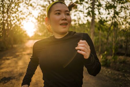 young happy Asian woman running in wood on sunset . Attractive and healthy Korean girl doing jogging...