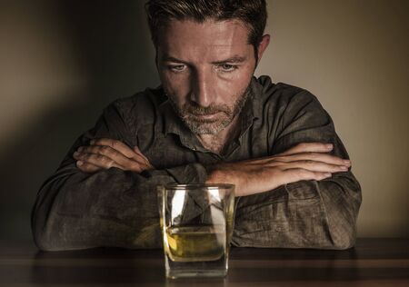 Attractive desperate alcoholic man . depressed addict isolated in front of whiskey glass trying not...