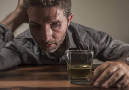alcoholic depressed and drunk addict man sitting in front of whiskey glass trying holding on drinking in dramatic expression suffering alcoholism and alcohol addiction on isolated backgroundの写真素材