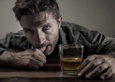 Attractive desperate alcoholic man . depressed addict isolated in front of whiskey glass trying not drinking in dramatic expression suffering alcoholism and alcohol addiction problemの写真素材