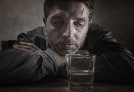 alcoholic depressed and drunk addict man sitting in front of whiskey glass trying holding on drinking in dramatic expression suffering alcoholism and alcohol addiction on isolated backgroundの写真素材