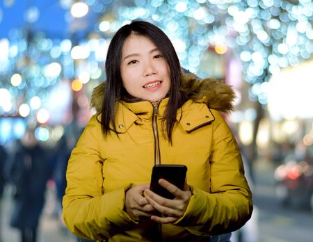 outdoors winter portrait of young beautiful and happy Asian Korean woman in warm hood jacket...