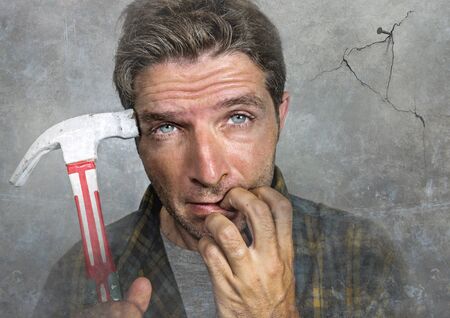 portrait of man holding hammer driving a nail for hanging a frame but making funny faces for the ...