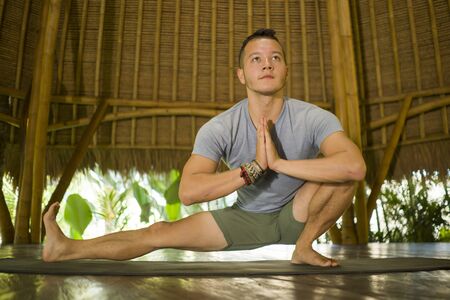 young attractive and happy man doing yoga drill and stretching exercise smiling relaxed in harmony at beautiful Asian bamboo hut enjoying nature in body mind balance and healthy lifeの写真素材