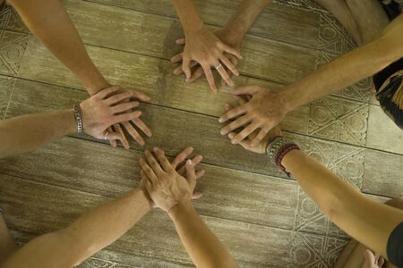 group of young hipster American friends enjoying Asian yoga retreat together sitting on lotus position holding hands on wooden hut floor meditating outdoors  in harmony and balanceの写真素材
