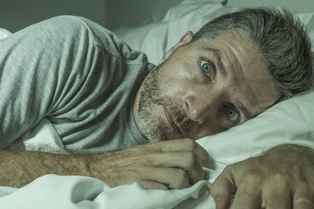 dramatic portrait of stressed and frustrated man in bed awake at night suffering insomnia sleeping disorder tired and desperate unable sleep feeling exhausted and sickの写真素材