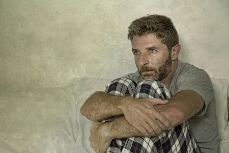 dramatic lifestyle portrait of young sad and depressed man lying thoughtful and pensive on bed looking away feeling lost thinking suffering some problem in sadness emotion and depression conceptの写真素材