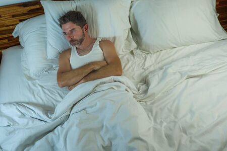 dramatic lifestyle portrait of young attractive sad and depressed man lying on bed awake thinking at night feeling stressed suffering depression problem in sadness and melancholy conceptの写真素材