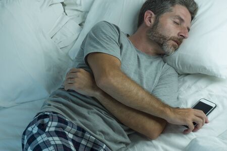 domestic lifestyle high angle portrait of young attractive and tired man sleeping on bed holding...