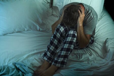 dramatic lifestyle portrait of young attractive sad and depressed man sitting on bed awake at night feeling stressed and desperate suffering depression problem in sadness and melancholy conceptの写真素材