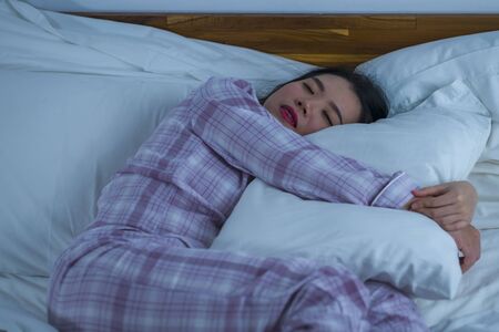 lifestyle portrait of young beautiful and sweet Asian Korean girl on her 20s alone at home sleeping relaxed wearing pajamas lying on bed happy and comfortable resting and dreamingの写真素材