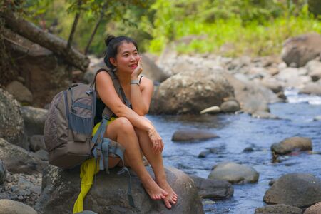 young beautiful and happy Asian Chinese woman carrying backpack trekking on mountains crossing river...