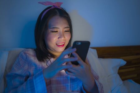 bedtime lifestyle portrait of young beautiful and happy sweet Asian Korean girl with bow headband...