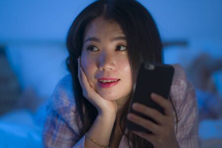bedtime lifestyle portrait of young beautiful and happy sweet Asian Korean woman with in pajamas...