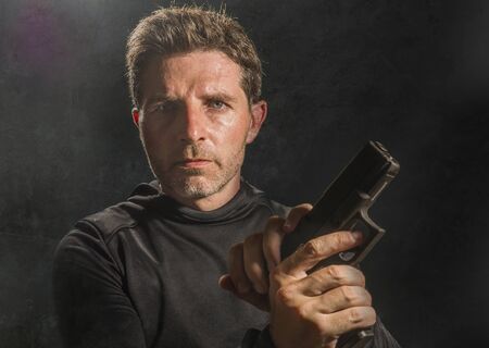 action portrait of serious and attractive hitman or special agent man holding gun reloading the...