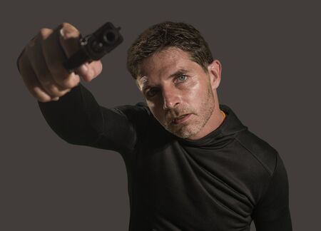 action portrait of angry and attractive hitman or special agent man holding gun pointing the handgun...