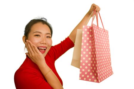 happy portrait of young beautiful and excited Asian Korean woman in red dress smiling excited holding shopping bags cheerful isolated on white background in beauty and fashion conceptの写真素材