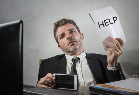 business lifestyle portrait of depressed and overwhelmed attractive man working at office computer desk in stress holding notepad as help sign feeling frustrated and exhaustedの写真素材