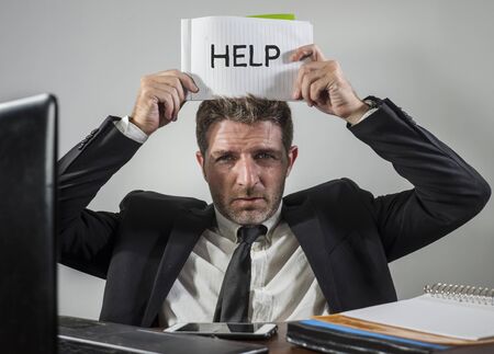 business lifestyle portrait of depressed and overwhelmed attractive man working at office computer desk in stress holding notepad as help sign feeling frustrated and exhaustedの写真素材