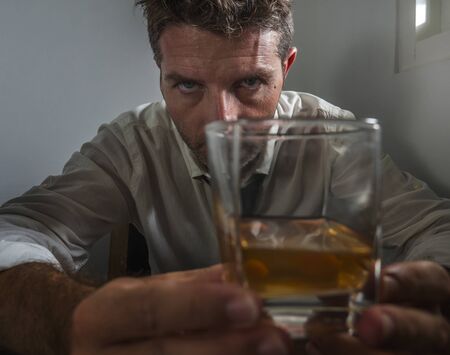 dramatic portrait of 30s to 40s alcoholic  man in lose necktie drinking alcohol desperate and wasted looking at whiskey glass thoughtful drunk and depressed fighting his drinking addictionの写真素材