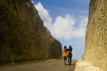 back view young happy and beautiful couple in love enjoying outdoors journey walking playful in cliff rock road exploring the landscape together in holidays travel adventure and wanderlustの写真素材