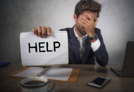 depressed and stressed attractive hispanic man in suit and tie working overwhelmed office computer desk holding notepad asking for help frustrated and overworked as businessman in troubleの写真素材