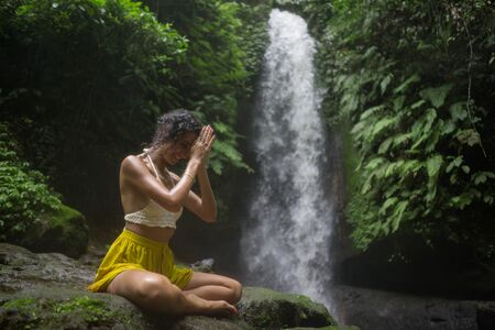 outdoors portrait of young attractive and happy hipster woman doing yoga at beautiful tropical waterfall meditating enjoying freedom and nature in healthy and zen lifestyleの写真素材