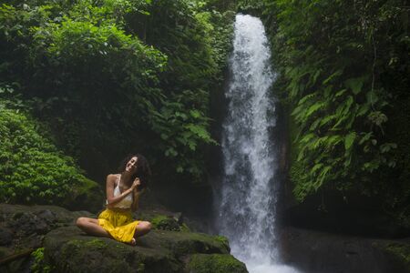 outdoors tropical lifestyle portrait of young attractive and happy hipster girl enjoying nature excited feeling free at amazing beautiful waterfall in exotic holidays travel destination and wanderlustの写真素材