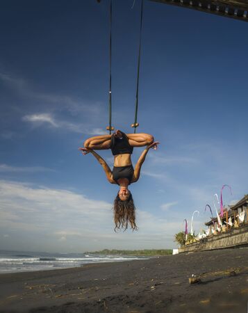 aero yoga beach workout - young attractive and athletic woman practicing aerial yoga exercise training acrobatic  body postures on blue sky over sea in Bali island healthy lifestyle concept
の写真素材
