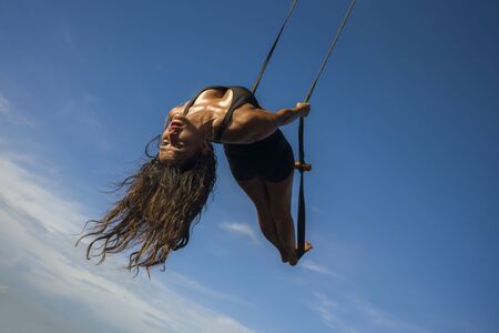aero yoga beach workout - young attractive and athletic woman practicing aerial yoga exercise...