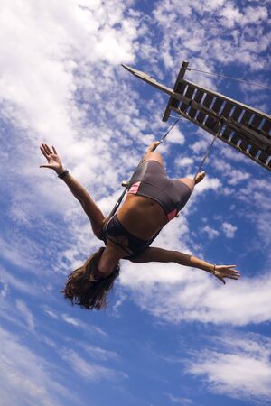 aerial yoga beach workout - young attractive and healthy woman practicing aero-yoga training balance body and mind control hanging from ropes above the sea isolated on beautiful blue skyの写真素材