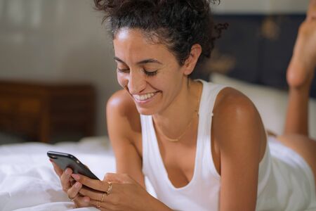 home lifestyle portrait of young happy and attractive hipster woman cozy on bed relaxed enjoying...
