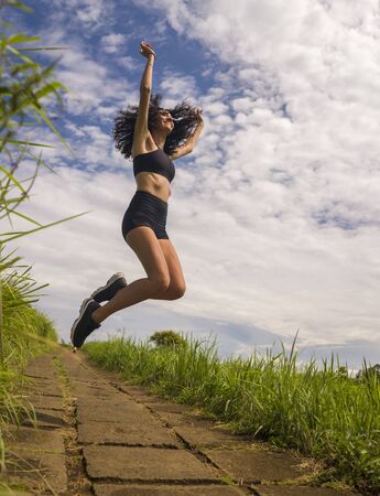 fresh and natural lifestyle portrait of young attractive and happy hipster woman with curly hair feeling free jumping on the air enjoying nature outdoors smiling cheerful and carefreeの写真素材