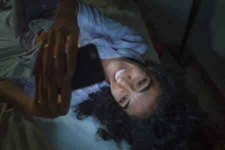 home lifestyle portrait of young happy and attractive hipster woman cozy on bed at night enjoying...