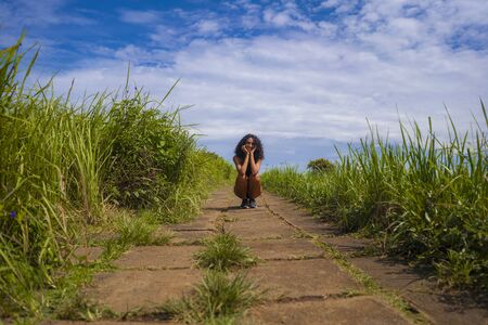fresh and natural lifestyle portrait of young attractive and happy hipster woman with curly hair in fitness clothes enjoying nature outdoors smiling cheerful sitting playful on countryside trackの写真素材