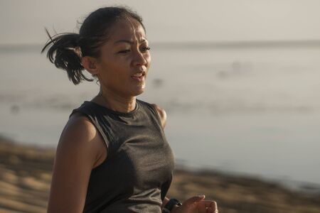 outdoors fitness portrait of young attractive and athletic Asian Indonesian woman in her 40s running on the beach doing intervals workout in athlete training concept and healthy lifestyleの写真素材
