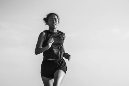 outdoors fitness portrait of young attractive and athletic Asian Indonesian woman in her 40s running on blue sky background doing intervals workout in athlete training and sport conceptの写真素材