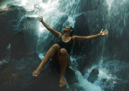 young attractive and blissful Asian Indonesian woman overwhelmed by the beauty of natural waterfall in tropical jungle enjoying happy the amazing and exotic travel destinationの写真素材