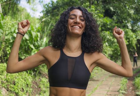 outdoors portrait of young happy and attractive hispanic woman with curly hair and athletic body...