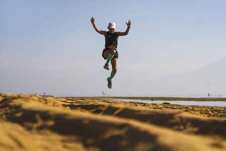 young athletic and attractive crazy happy woman jumping high on the air at beautiful beach enjoying...