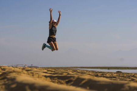 young athletic and attractive crazy happy woman jumping high on the air at beautiful beach enjoying...